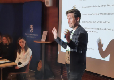 Micke Larsson håller presentation framför powerpoint, i bakgrunden syns Sanna Marin