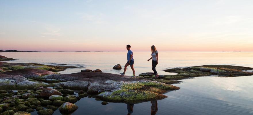 Två personer som går på en klippa vid vattnet i solnedgång