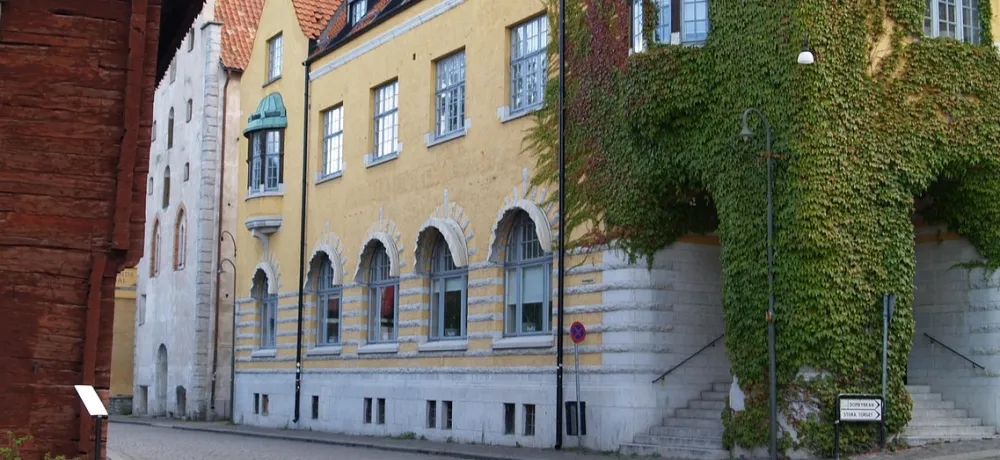 Bild på en gata i Visby, ett gult stenhus och hörnet av ett rött stockhus